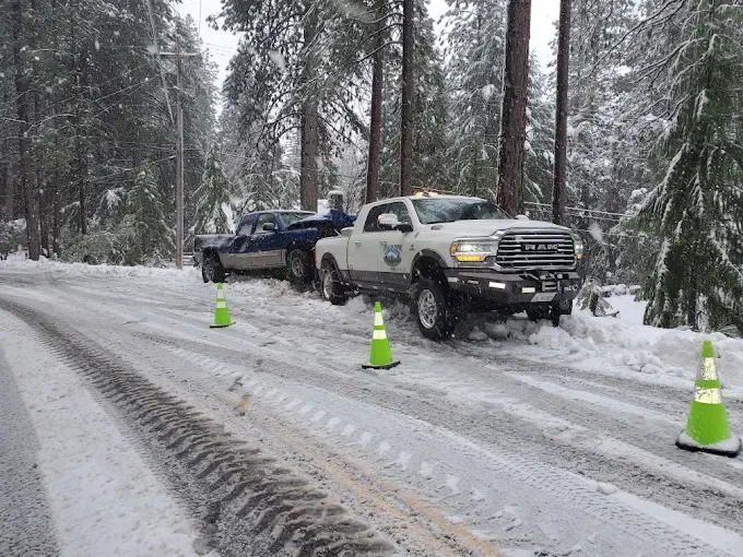 Ridgeline Towing truck with safety cones pulling a car out of the snow on a mountain road