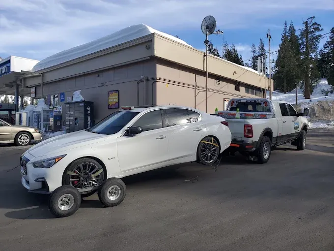 Sedan on tow dollies behind a Ridgeline Towing truck at a snowy Sierra gas station