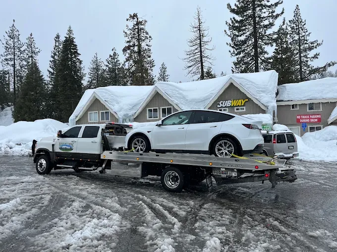 Ridgeline Towing flatbed hauling a white SUV through deep snow in the Sierra Nevada